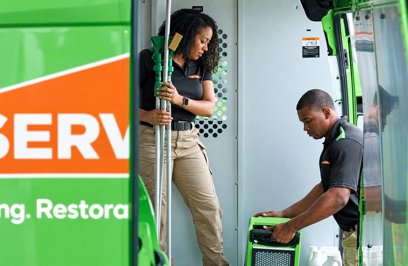 SERVPRO technicians unloading drying equipment from a green response van